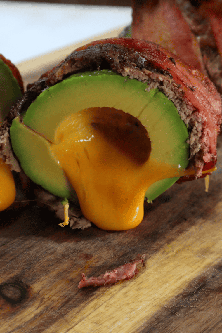 Crispy air fryer bacon-wrapped avocado burger bombs sliced open to reveal melted cheddar and creamy avocado inside