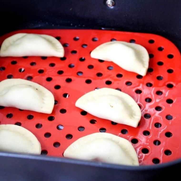 Unbaked blueberry goat cheese empanadas brushed with egg wash and sprinkled with turbinado sugar, arranged in a single layer in an air fryer basket