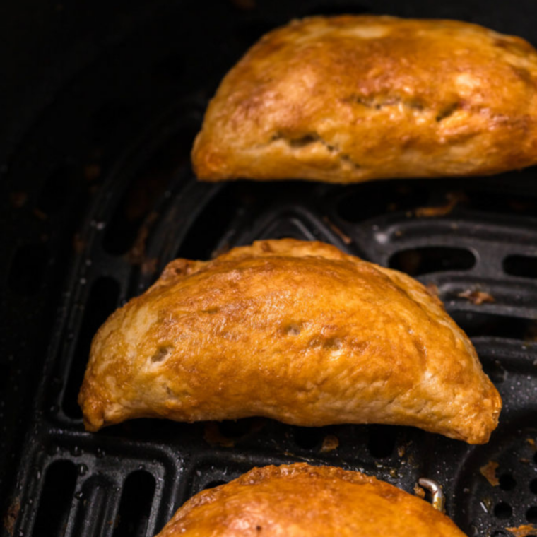 Golden brown blueberry goat cheese empanadas in an air fryer basket after cooking, crimped edges crisp and sugar-topped