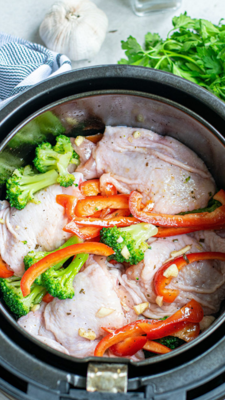 Chicken thighs and vegetables arranged in the air fryer basket before cooking.