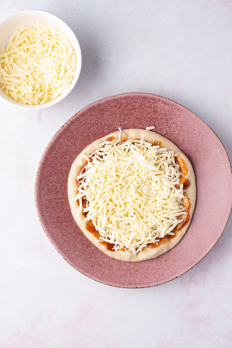Spreading pizza sauce onto pita bread with a spoon, leaving a half-inch border around the edge for the crust