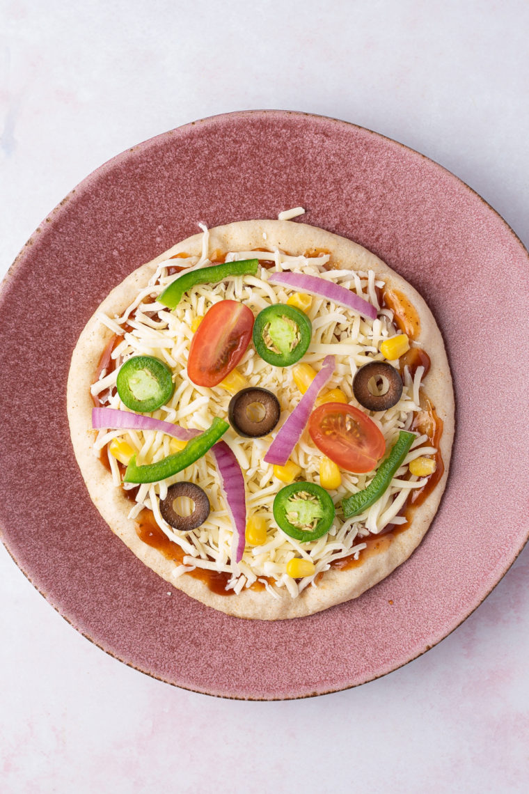 Sprinkling shredded mozzarella cheese onto pita pizza before adding pepperoni and vegetable toppings