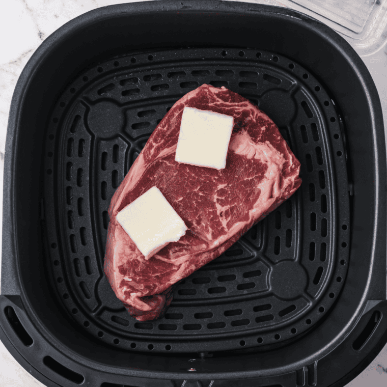 Placing ribeye steak in air fryer basket to cook, flipping halfway through.