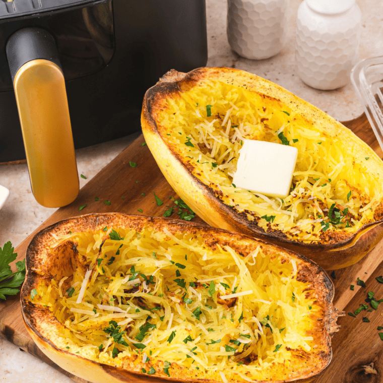 Air fryer spaghetti squash halves with browned edges on a wooden cutting board.
