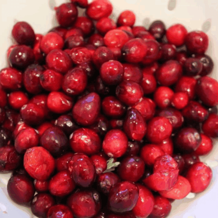 Fresh cranberries being rinsed under cold water in a colander, with stems and debris removed.