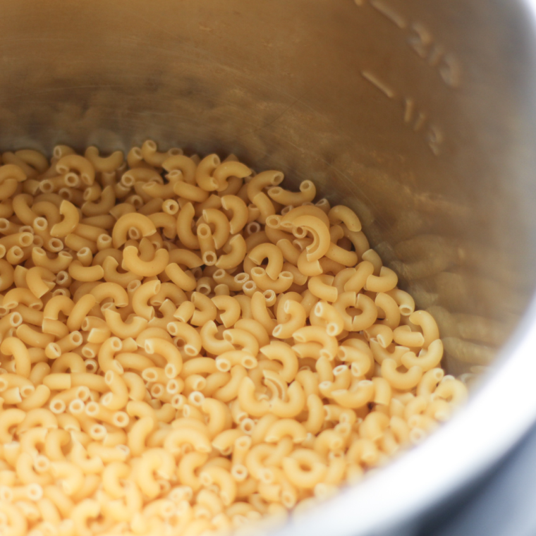 All ingredients for Instant Pot Panera Mac and Cheese laid out on a countertop, including elbow macaroni, sharp cheddar cheese, American cheese, butter, milk, vegetable broth, Dijon mustard, and hot sauce.