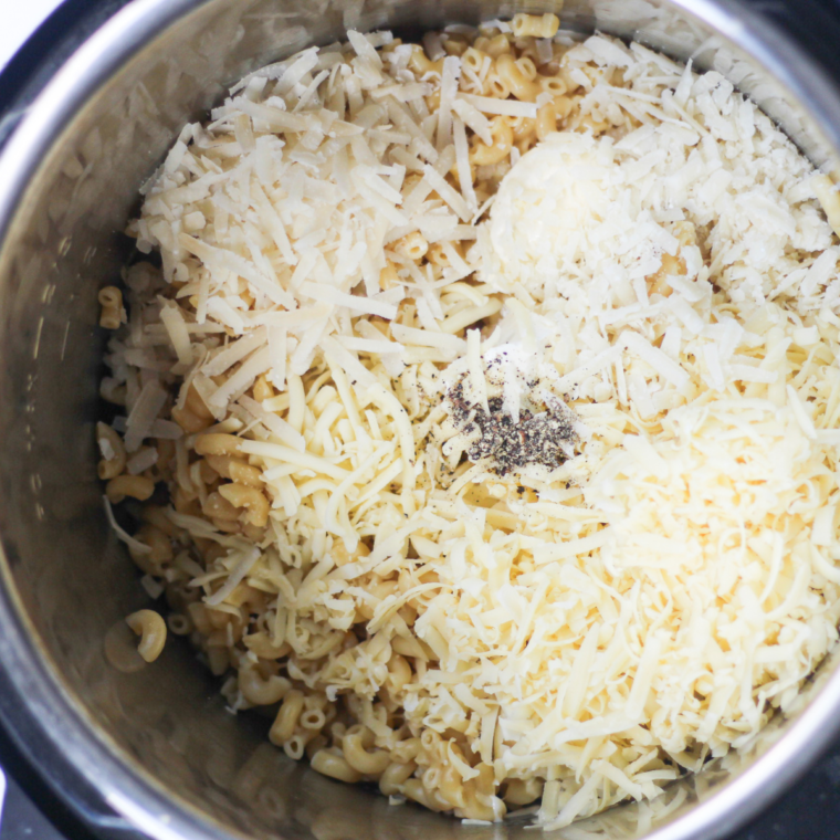 Melted butter and a mix of sharp cheddar and American cheese being stirred into the cooked macaroni inside the Instant Pot.