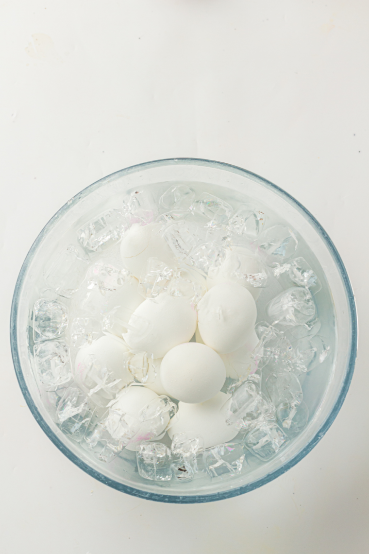Hard-boiled eggs being transferred from the Instant Pot into a glass bowl of ice water to stop cooking and prevent green yolks