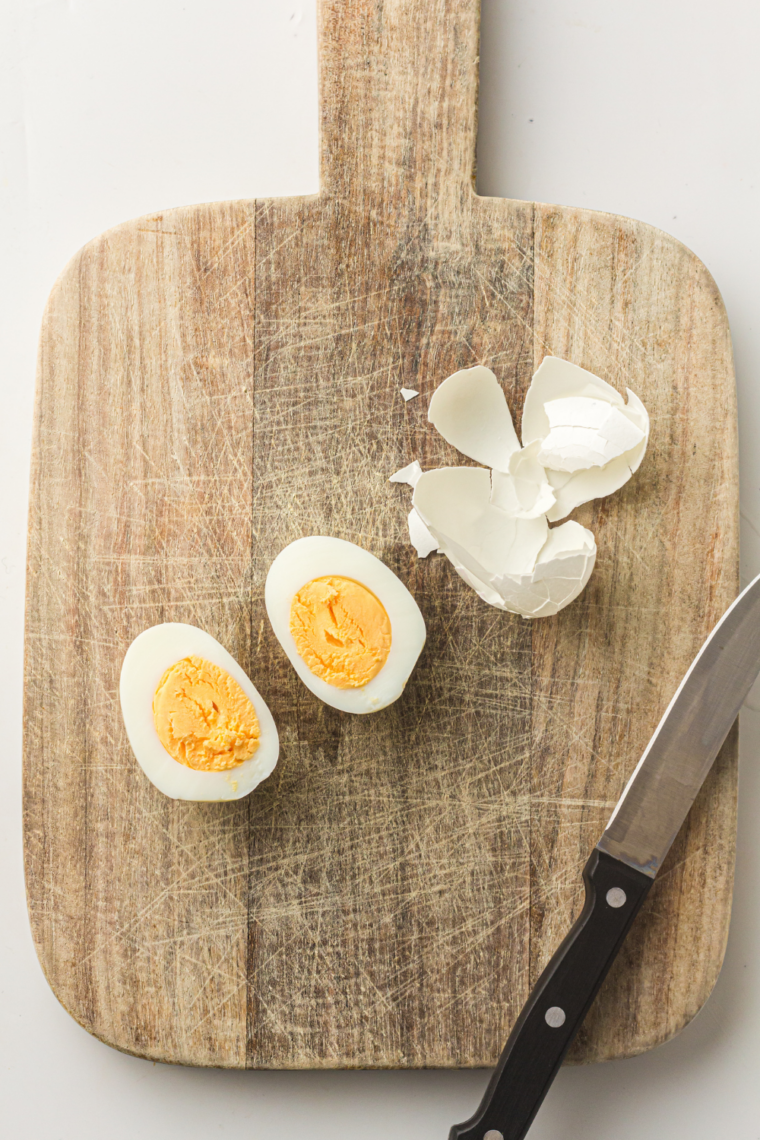Peeled hard-boiled eggs sliced in half lengthwise on a cutting board with yellow yolks being scooped into a mixing bowl