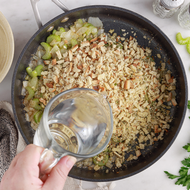 Fork fluffing herb stuffing mix moistened with chicken broth and melted butter in a pot