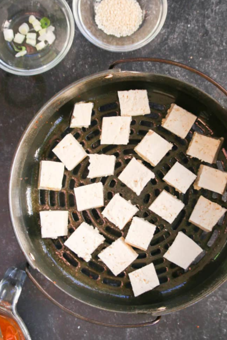 Air fryer basket filled with golden-brown salt and pepper tofu.