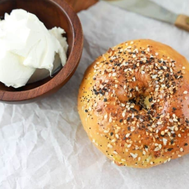 Whole everything bagel with a container of cream cheese next to the bagel.