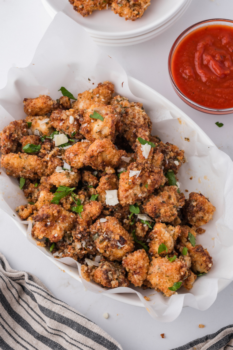 Air fryer basket of crispy garlic parmesan chicken bites with a bowl of dipping sauce on the side