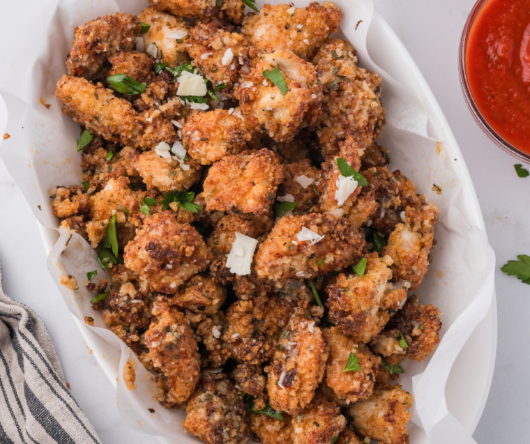 Crispy chicken bites in an air fryer basket next to a bowl of garlic butter parmesan sauce