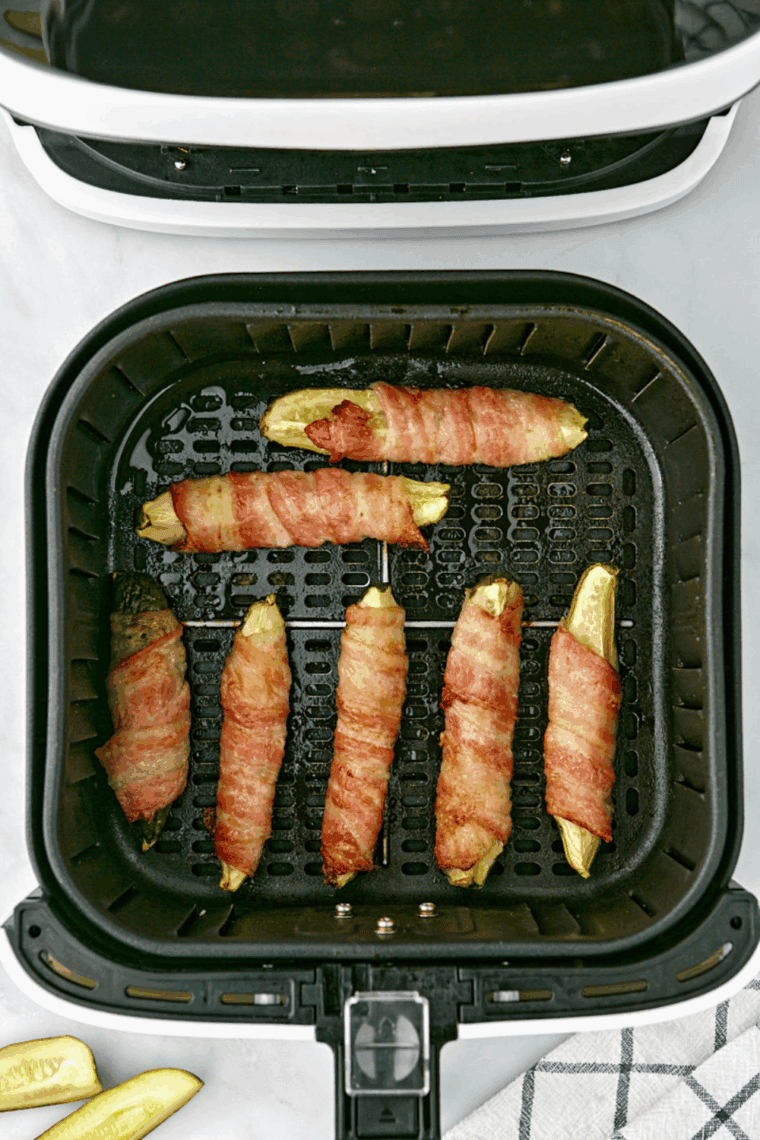 Air fryer bacon wrapped pickles on a basket, crispy golden bacon with dill pickles inside, ready to serve.