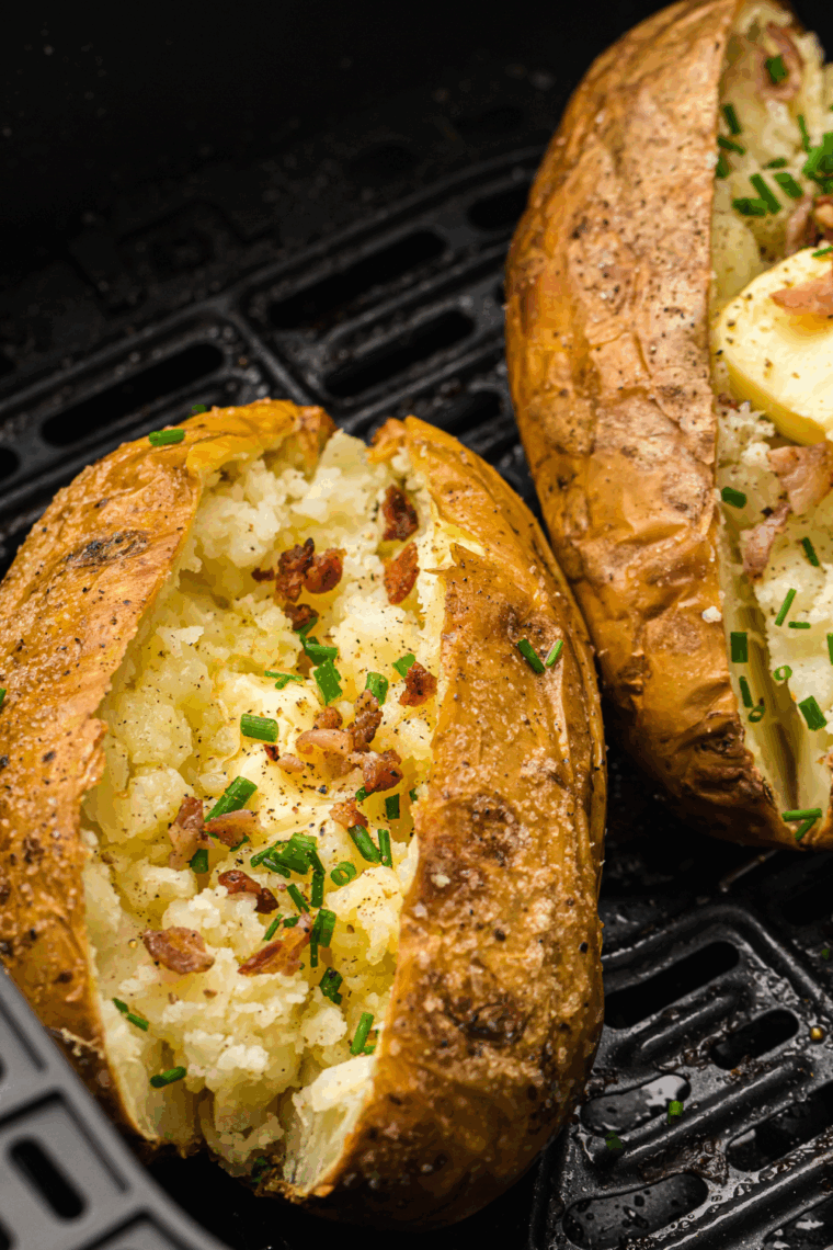 Crispy salt-crusted baked potatoes sliced open with fluffy centers, topped with butter, sour cream, and chives on a white plate.