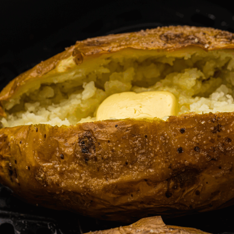Fluffy baked potatoes with crispy, seasoned skins topped with sour cream and chives on a white plate.