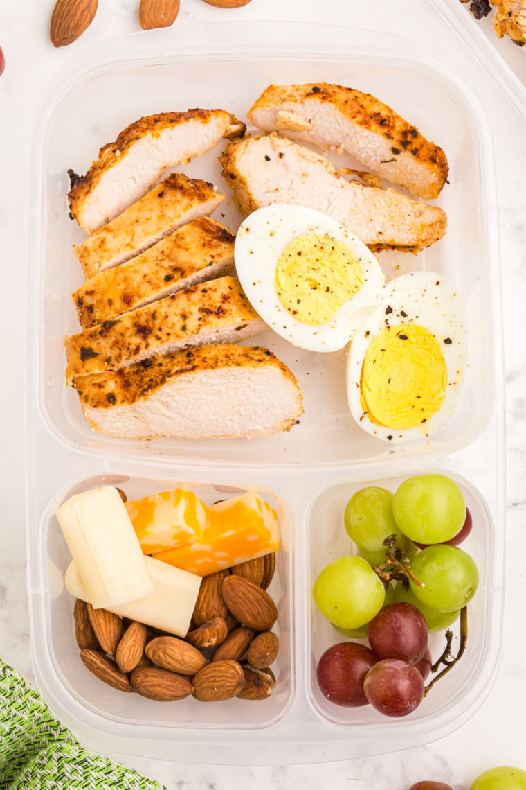 Copycat Starbucks protein box with sliced air fryer chicken, a hard-boiled egg, cheddar cubes, grapes, and almonds in a compartment container