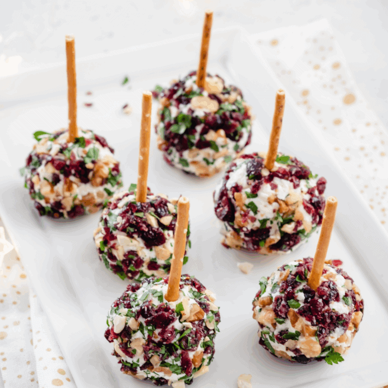 Festive Cranberry Pecan Cheese Ball on a plate, coated with chopped pecans and fresh herbs.