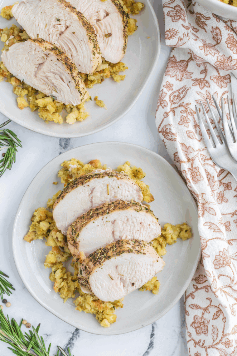 Golden brown air fryer turkey tenderloin sliced on a plate, served with herbs and vegetables.
