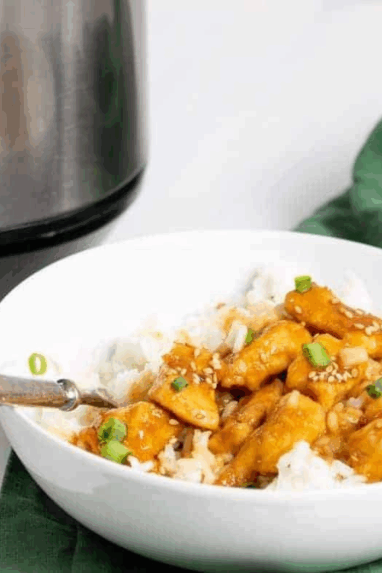 Crispy sesame chicken coated in sticky sauce, garnished with sesame seeds and green onions on a plate.