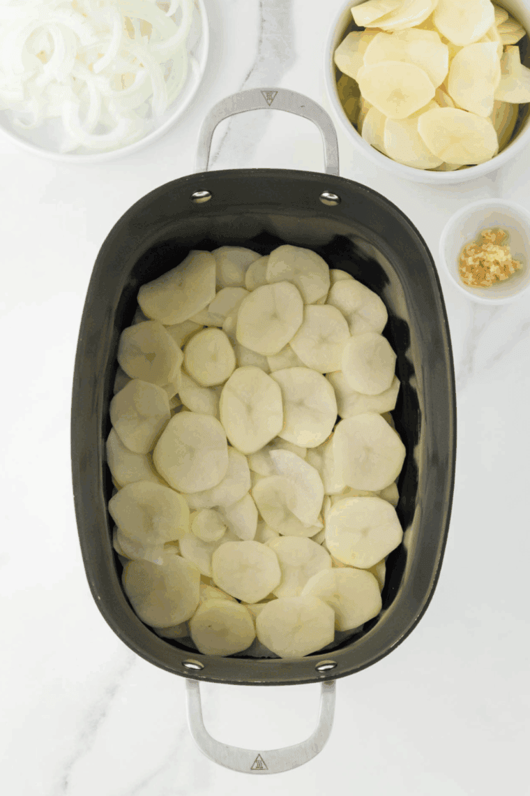 Layering sliced potatoes, creamy sauce, and shredded cheeses in a sprayed crockpot