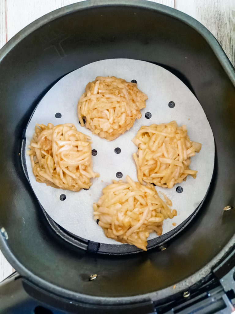 Top view of uncooked Air Fryer Latke patties on the bottom of an air fryer basket that is covered in greaseproof paper with holes in it. 