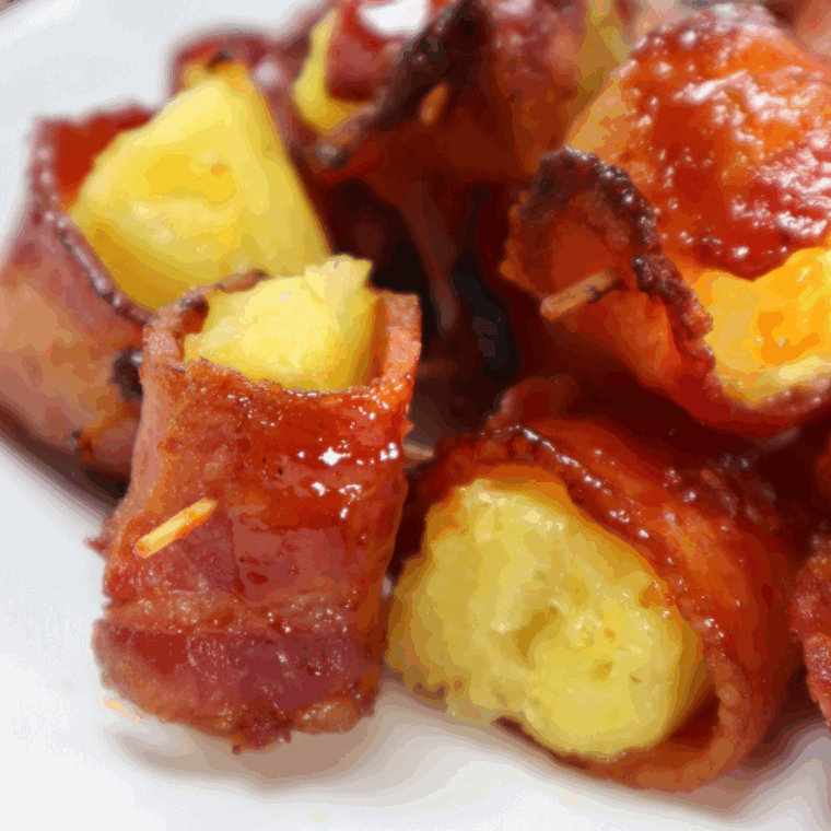 Crispy bacon wrapped around juicy pineapple chunks, cooked in the air fryer and served on a plate.