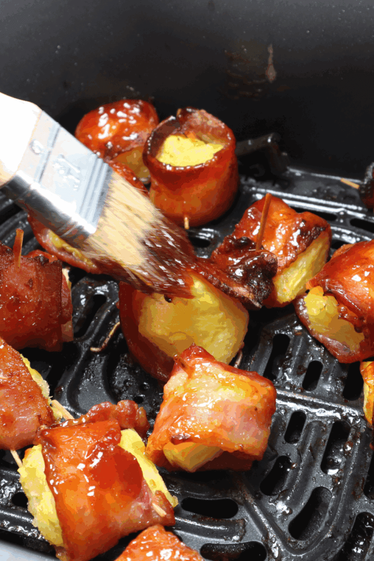 Golden, crispy bacon-wrapped pineapple bites fresh from the air fryer, served on a white platter.