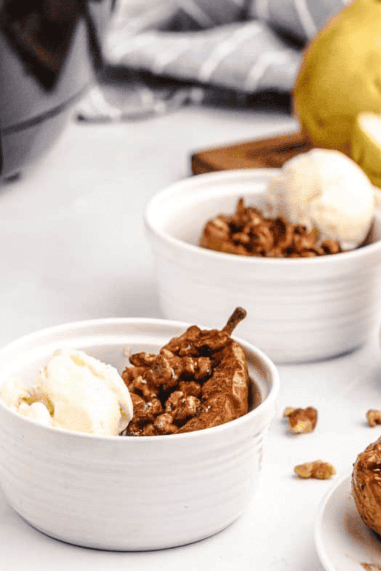 Air fryer baked pears topped with cinnamon, chopped nuts, honey, and vanilla ice cream served in white ramekins