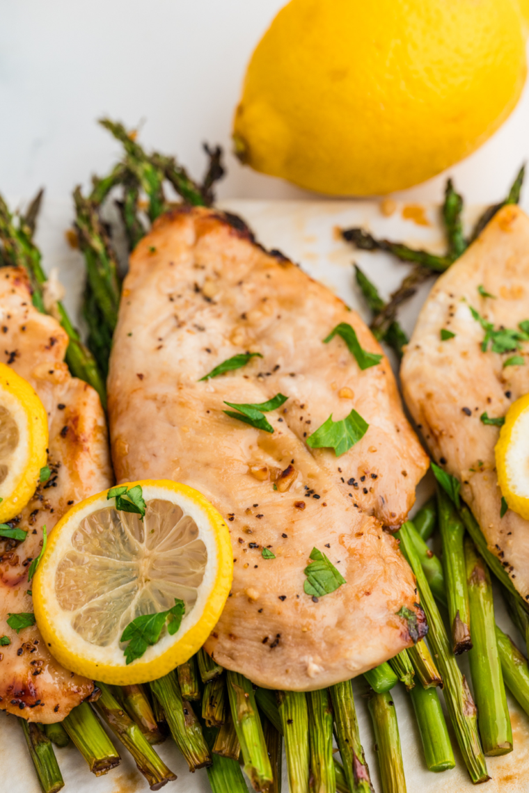 Close-up of seasoned chicken breasts and asparagus spears in the air fryer basket.