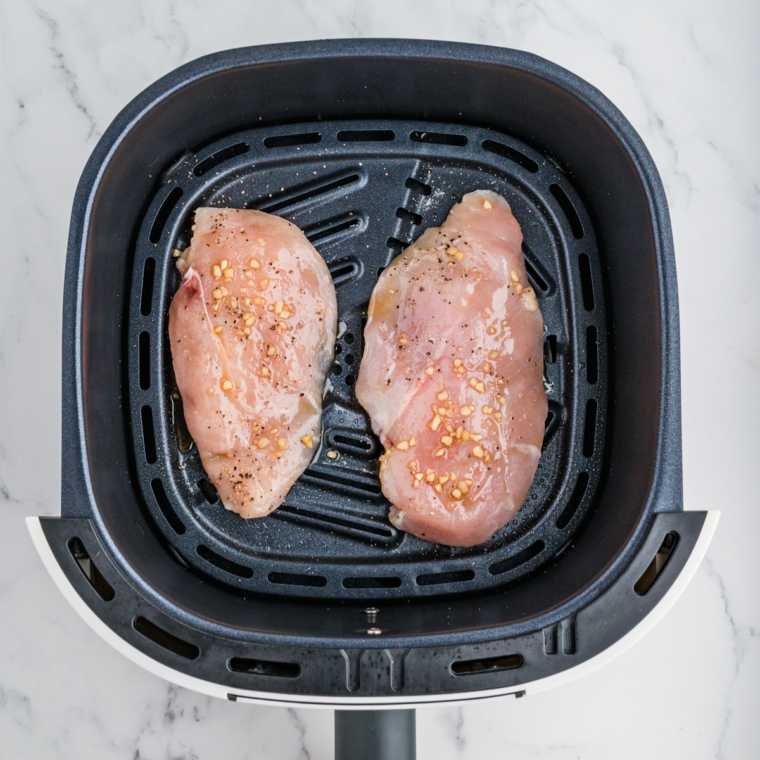 Seasoned chicken breast in the air fryer basket.