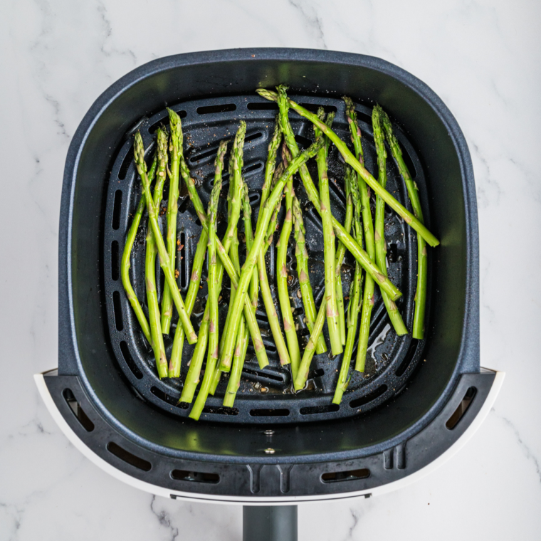 Asparagus cooking in the air fryer basket.