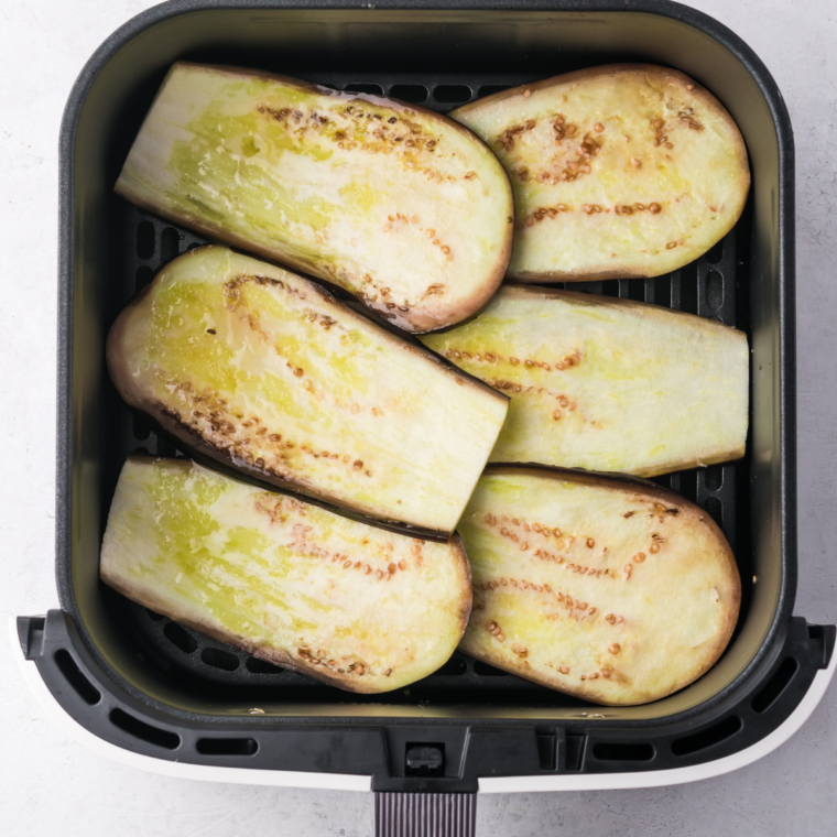 Eggplant slices brushed with olive oil in an air fryer basket, cooking at 350°F until tender.