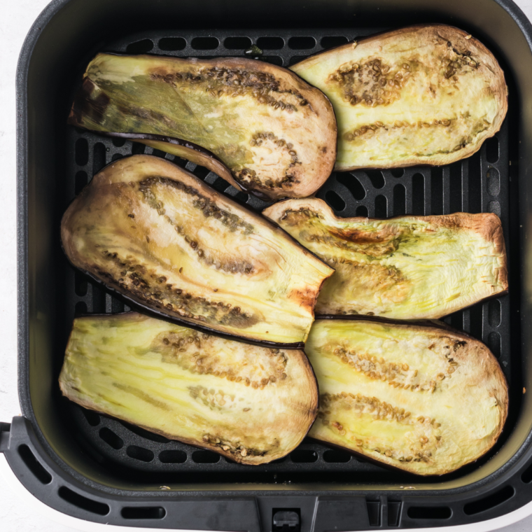 Eggplant slices in an air fryer basket, brushed with olive oil and cooking at 350°F for 6-8 minutes until tender.