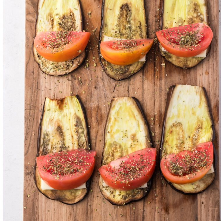 Adding mozzarella, tomato, oregano, and basil on top of air-fried eggplant slices for Air Fryer Eggplant Rollatini.