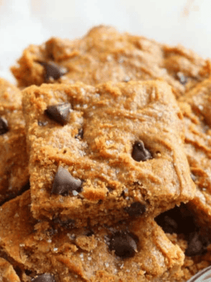 Sliced air fryer flourless peanut butter blondies stacked on parchment paper with chocolate chips