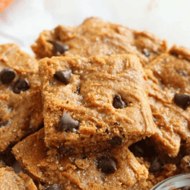 Sliced air fryer flourless peanut butter blondies stacked on parchment paper with chocolate chips