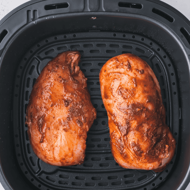 Pouring balsamic Dijon marinade over seasoned chicken in an air fryer pan