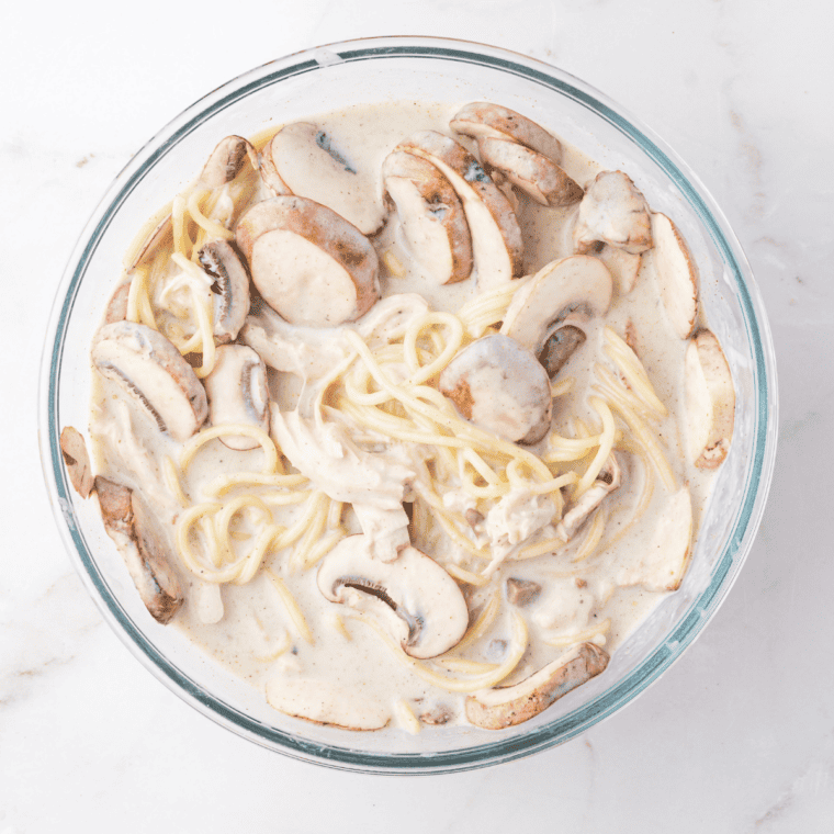 Cooked spaghetti and turkey mixed together with creamy tetrazzini sauce in a large bowl.