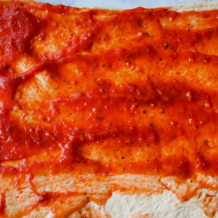 Marinara sauce spread on dough with mozzarella cheese and pepperoni slices on top.