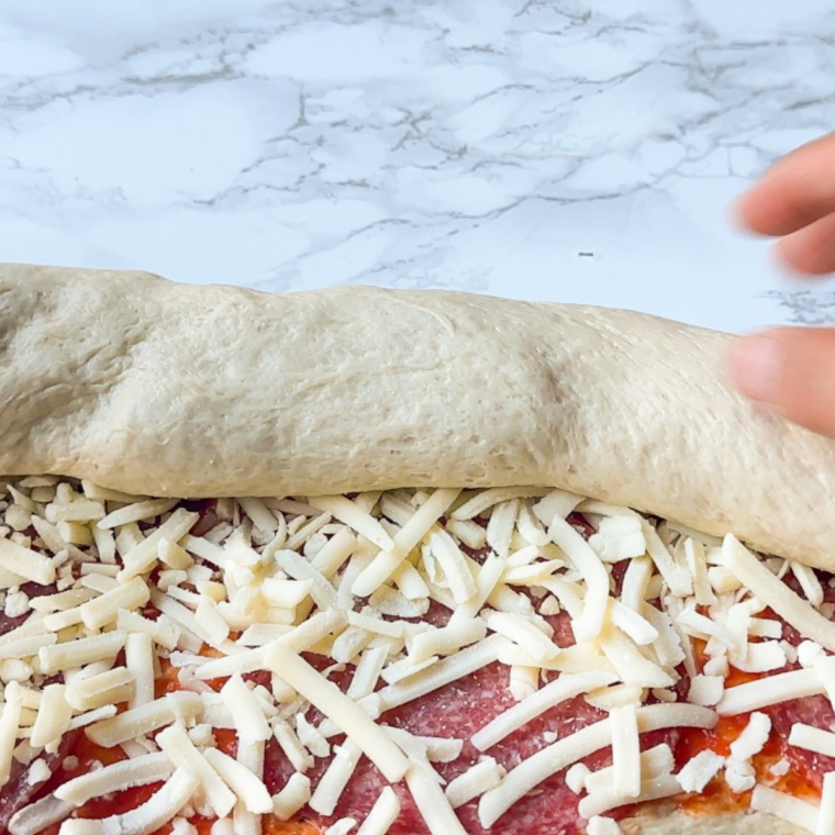 Dough being rolled into a log and cut into individual pizza rolls.