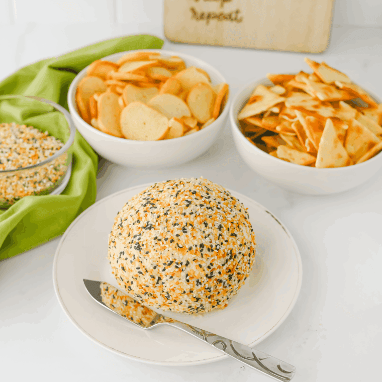Everything Bagel Cheese Ball coated with bagel seasoning, served with crackers and fresh vegetables for dipping.