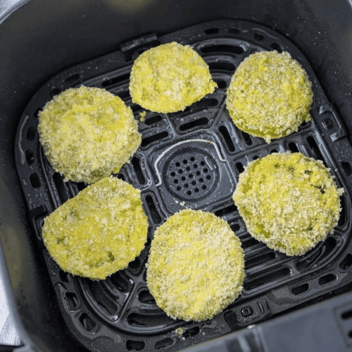 Top view of square Air Fryer basket with six uncooked breaded green tomatoes in it. 