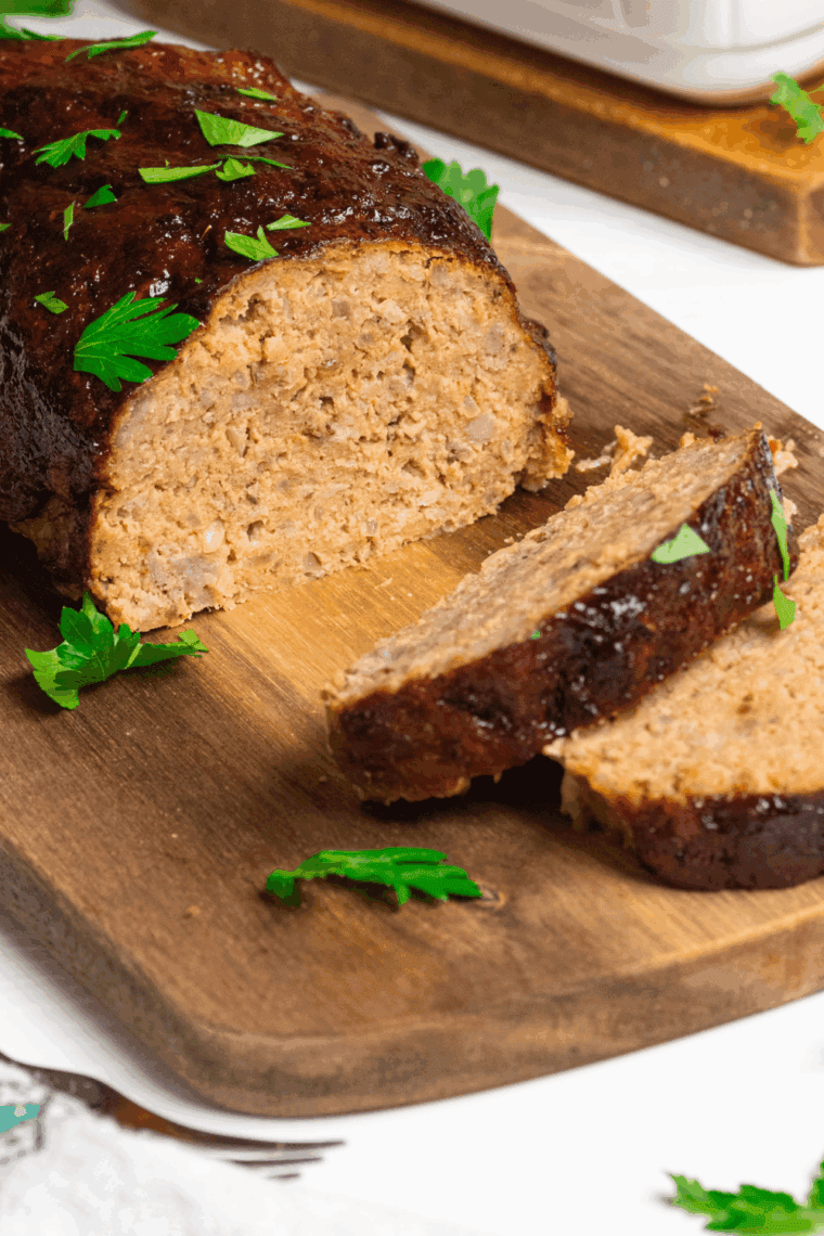 Slice of moist meatloaf made without eggs, served on a plate with vegetables.