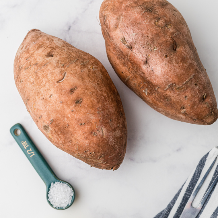 Freshly scrubbed sweet potatoes pierced with a fork, ready for cooking.