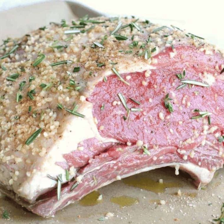 Prime rib being seasoned with olive oil, salt, black pepper, smoked paprika, garlic powder, crushed garlic, and fresh rosemary and thyme for a flavorful roast.