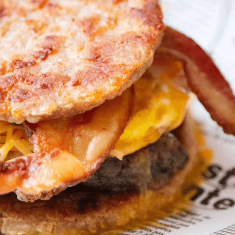 Keto copycat sausage McGriddle cut in half showing the sausage patty, fried egg and melted cheese between two golden fathead dough buns