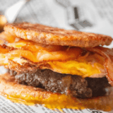 Keto copycat sausage McGriddle cut in half showing the sausage patty, fried egg and melted cheese between two golden fathead dough buns