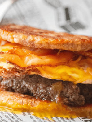 Keto copycat sausage McGriddle cut in half showing the sausage patty, fried egg and melted cheese between two golden fathead dough buns
